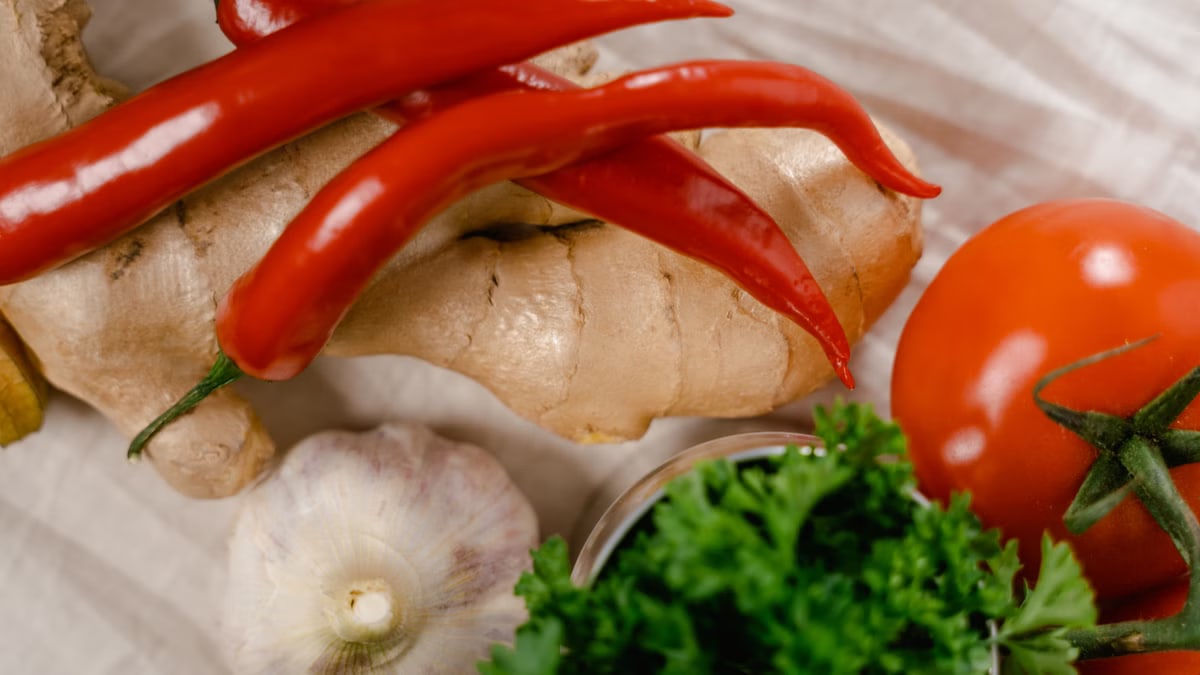 Close-up of fresh ingredients including chili peppers, ginger, and tomatoes on a white fabric surface.